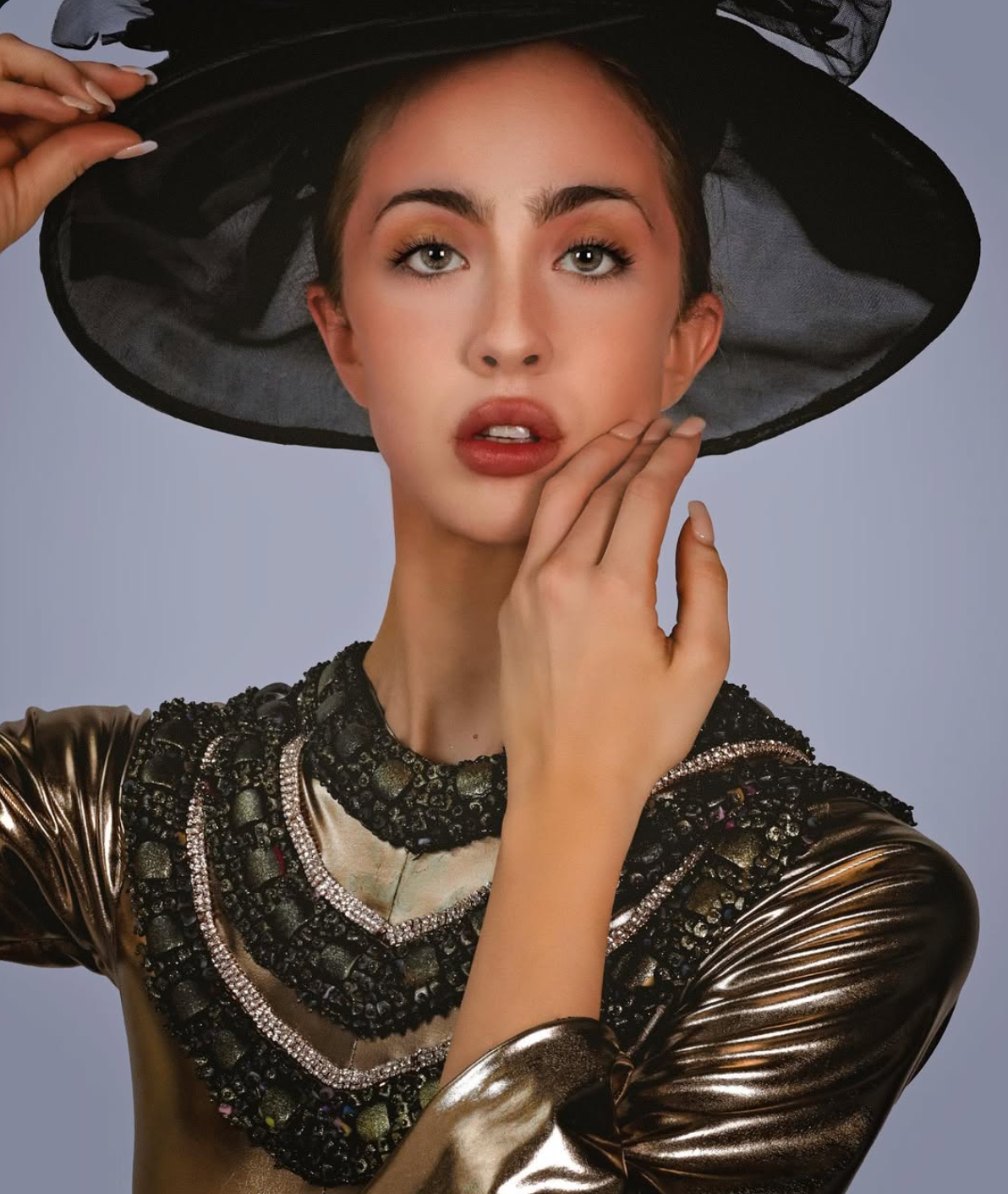 Kristin in a wide-brim black hat and a beaded gold jacket